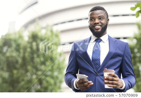 Handsome businessman standing outdoors with coffee and smartphone in arms 57070909