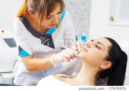 Pretty Caucasian female having of hyaluronic acid injection in face zone. Male doctor with syringe Pretty Caucasian female having of hyaluronic acid injection in face zone. Male doctor with syringe 57070976