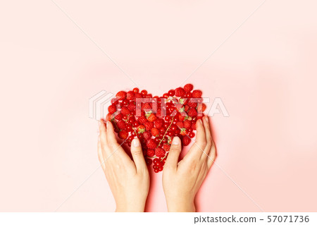 Female hands and red berries in the shape of a Female hands and red berries in the shape of a 57071736