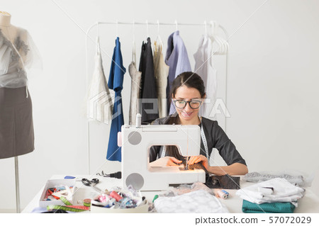 Dressmaker, tailor and fashion concept - Smiling female fashion designer using sewing machine and Dressmaker, tailor and fashion concept - Smiling female fashion designer using sewing machine and 57072029