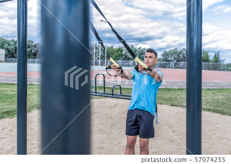 Athlete man, trains in the summer in the city, in hands of loops, sports straps for push-ups and Athlete man, trains in the summer in the city, in hands of loops, sports straps for push-ups and 57074255