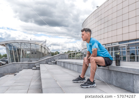Athlete man sits and rests after tough summer workout in city. Free space for text. Sportswear T 57074287