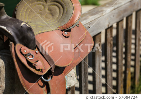 Old worn leather horse saddle on wooden fence, lit 57084724