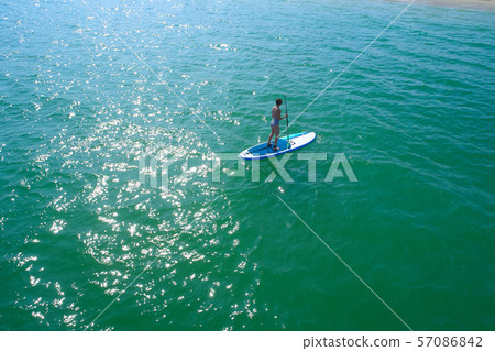 Aerial drone birds eye view of young woman exercising sup board in turquoise tropical clear waters Aerial drone birds eye view of young woman exercising sup board in turquoise tropical clear waters 57086842