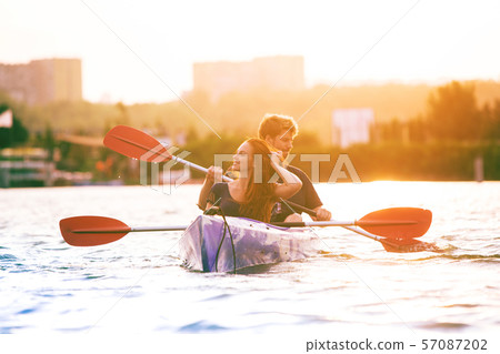 Confident young couple kayaking on river together with sunset on the background Confident young couple kayaking on river together with sunset on the background 57087202