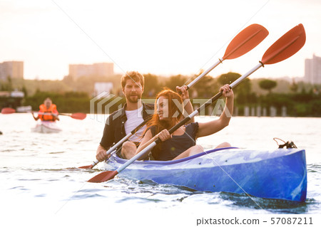 Confident young couple kayaking on river together with sunset on the background Confident young couple kayaking on river together with sunset on the background 57087211