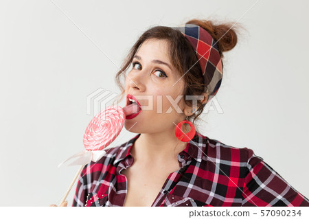 Close up portrait of beautiful young woman eating lollipop over white background Close up portrait of beautiful young woman eating lollipop over white background 57090234