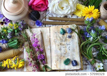 Witch spell book, calendula, rose flowers, reiki crystals and candles on wooden table 57090329