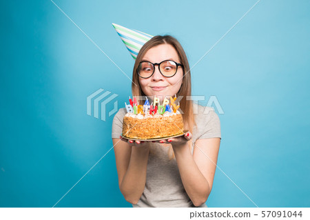 Crazy funny girl in a paper hat and glasses holding a big birthday cake on the blue background 57091044