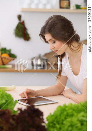 Young woman looking for a new recipe for cooking in a kitchen. Housewife is making online shopping 57091314