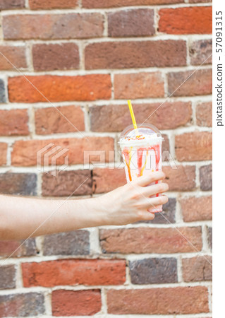The hand of an unidentified young man holds in his hands a milky fruit berry cocktail against a 57091315