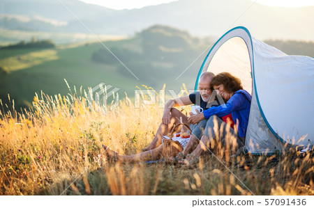 Senior tourist couple in love sitting in nature at sunset, resting. Senior tourist couple in love sitting in nature at sunset, resting. 57091436
