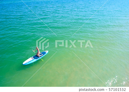 Young woman paddling on SUP board on the tropical beach. Active summer vacations with paddle board. Young woman paddling on SUP board on the tropical beach. Active summer vacations with paddle board. 57101532