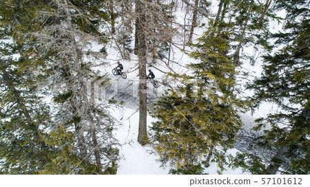 Aerial view of two mountain bikers riding on road in forest outdoors in winter. 57101612