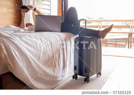 Relaxed businessman lying in bed looking at cellphone with laptop on his lap. 57103128
