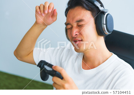 Image of e-sports: A scene in which a young man has a disappointing expression when playing a game with a controller in one hand Image of e-sports: A scene in which a young man has a disappointing expression when playing a game with a controller in one hand 57104451