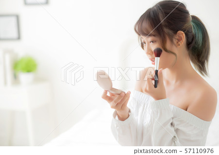 Beauty portrait young asian woman smiling with face looking mirror applying makeup with brush cheek Beauty portrait young asian woman smiling with face looking mirror applying makeup with brush cheek 57110976
