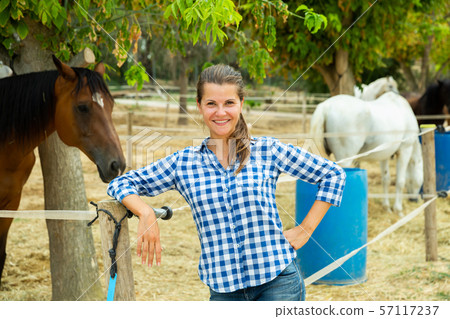 Positive female farmer who is standing near corral at the farm Positive female farmer who is standing near corral at the farm 57117237
