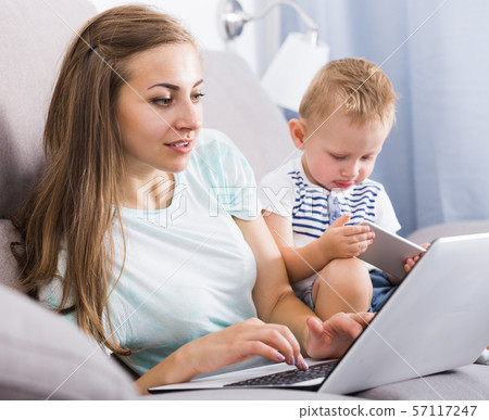 Satisfied female 22-27 years old is productively working behind laptop while child playing on tablet 57117247