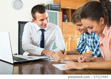 Agent with laptop and young couple. Agent with laptop and young couple. 57117497