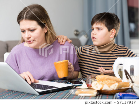 Young woman working at laptop and son trying to talking with she 57117917