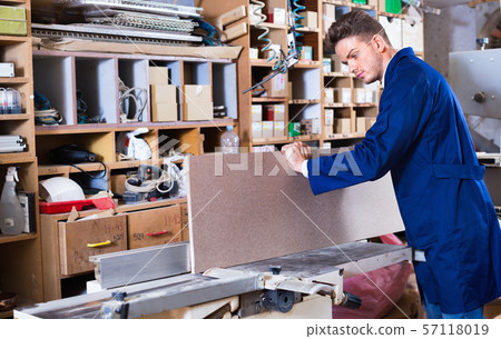 Positive guy fixing chipboard on table at workshop 57118019