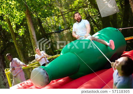 Joyful man saddling inflatable rodeo bottle 57118305