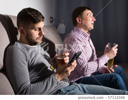 Bored guy with phone while friend watching tv 57118306