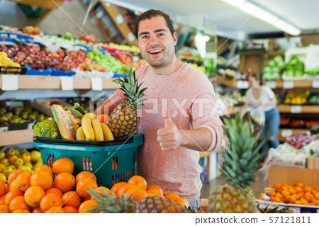 Cheerful man standing with full shopping cart during shopping 57121811