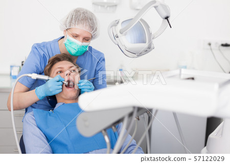Male patient sitting on chair in dental office getting dentist treatment Male patient sitting on chair in dental office getting dentist treatment 57122029