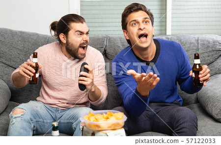 Two men watching matchup on tv drinking beer together at home 57122033