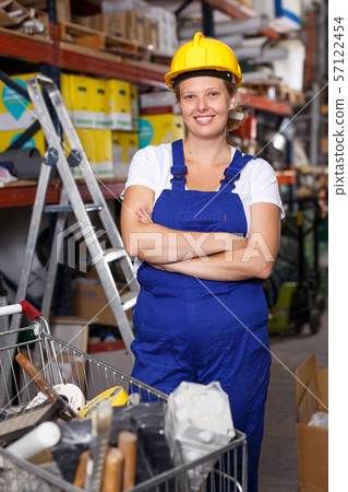 Female in helmet standing near shelves with construction materials in build shop 57122454