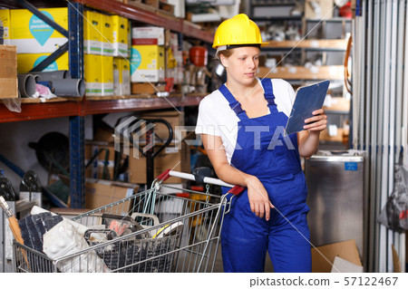 Young woman customer in helmet with notebook looking construction materials Young woman customer in helmet with notebook looking construction materials 57122467