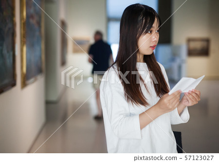 Chinese female visitor with guide-book looking at artwork painting 57123027
