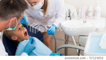 Male stomatologist with girl assistant are diagnosticating to young patient which is sitting Male stomatologist with girl assistant are diagnosticating to young patient which is sitting 57123052