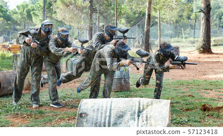 Team of adult people playing paintball on battlefield outdoor, running with guns Team of adult people playing paintball on battlefield outdoor, running with guns 57123418