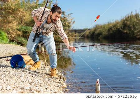 Adult man standing near river and pulling fish expressing emotions of dedication 57123610