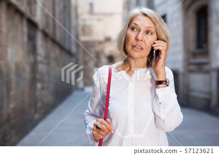Smiling mature female is walking and talking by phone 57123621