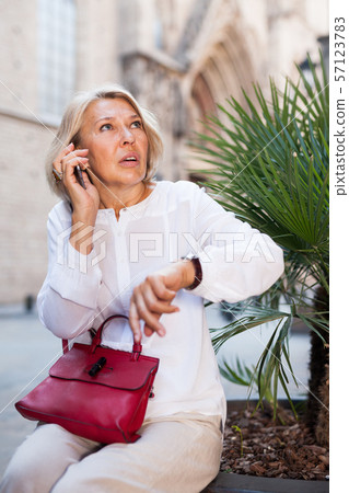Hurrying woman looks at her watch and talking on the phone 57123783