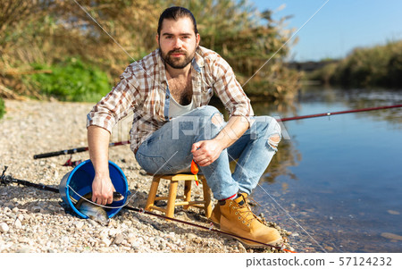 Bearded adult man posing with fish near river in summertime Bearded adult man posing with fish near river in summertime 57124232