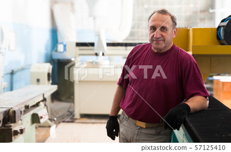 Portrait of elderly foreman in protective gloves standing in workshop Portrait of elderly foreman in protective gloves standing in workshop 57125410