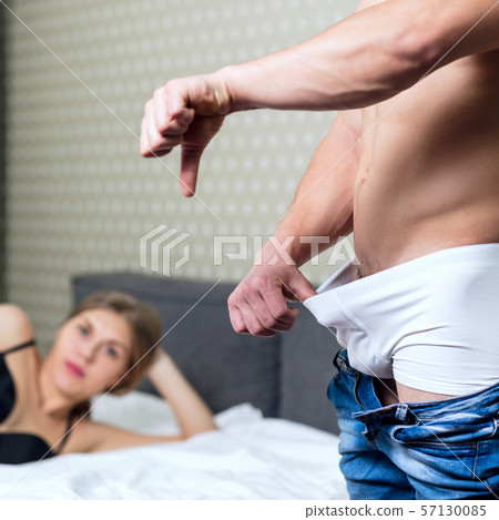 Young man looking in underpants and shows thumbs down gesture. Young man looking in underpants and shows thumbs down gesture. 57130085