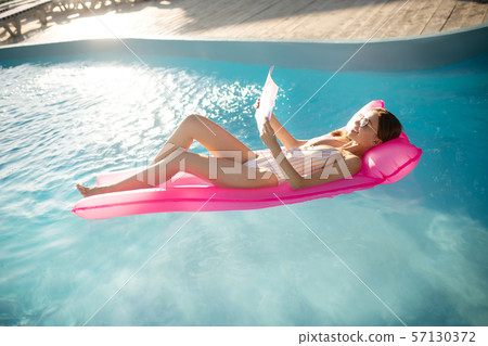 Woman reading magazine while lying on air bed in pool 57130372