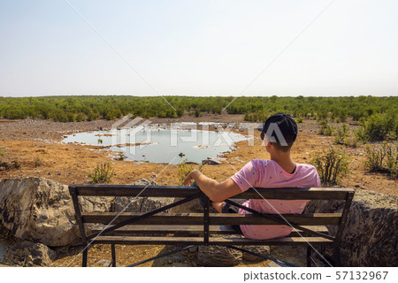 Tourist waits for wildlife at the Moringa waterhole near Halali, Etosha, Namibia 57132967