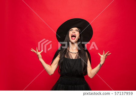 Young woman in hat and dress as a witch on red background Young woman in hat and dress as a witch on red background 57137959