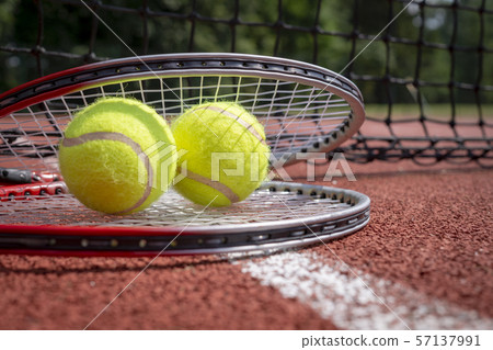 Two tennis balls resting on top of tennis racquet 57137991