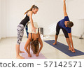 Woman in yoga studio adjusts student in Mysore style ashtanga class. Female teacher with young yogis. Man in utthita trikonasana, known as extended triangle pose. Healthy workout, exercise concepts 57142571