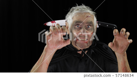 Elderly man with knife in head. Halloween makeup and costume. Blood on his face Elderly man with knife in head. Halloween makeup and costume. Blood on his face 57148634