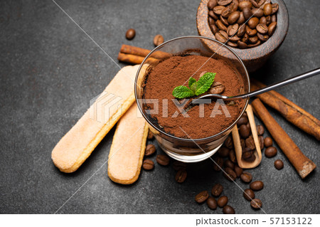 Portion of Classic tiramisu dessert in a glass cup, scoop full of coffee and cinnamon sticks on dark Portion of Classic tiramisu dessert in a glass cup, scoop full of coffee and cinnamon sticks on dark 57153122