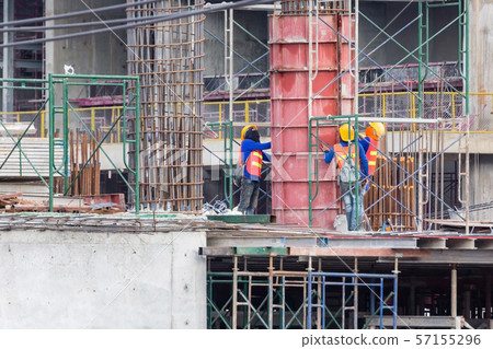 Worker making framework for concrete pillar with metal rods for building construction. 57155296
